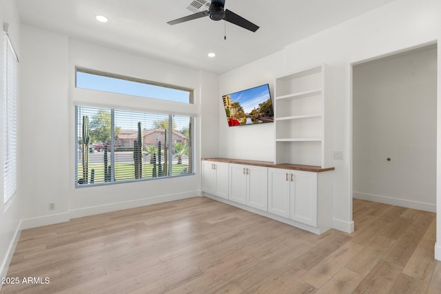 empty room with built in shelves, ceiling fan, and light hardwood / wood-style floors