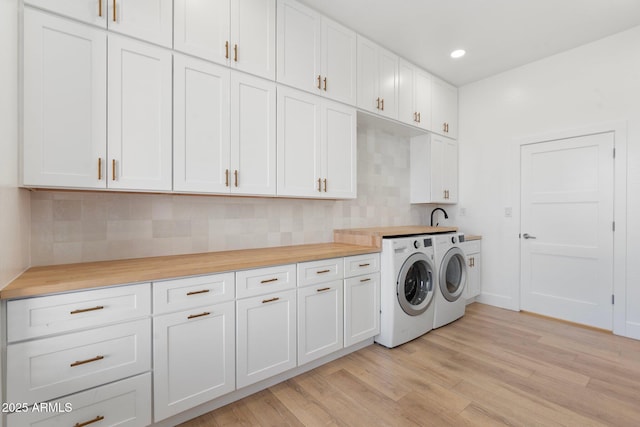 laundry area with light hardwood / wood-style floors, washing machine and dryer, and cabinets