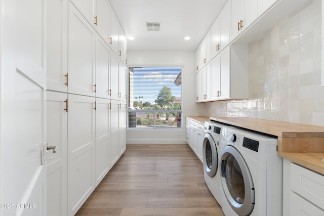 clothes washing area with cabinets, light hardwood / wood-style floors, and washing machine and dryer