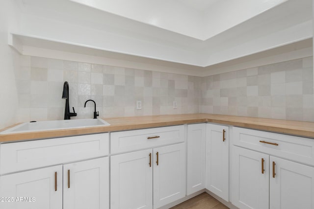 kitchen with butcher block counters, sink, decorative backsplash, and white cabinets