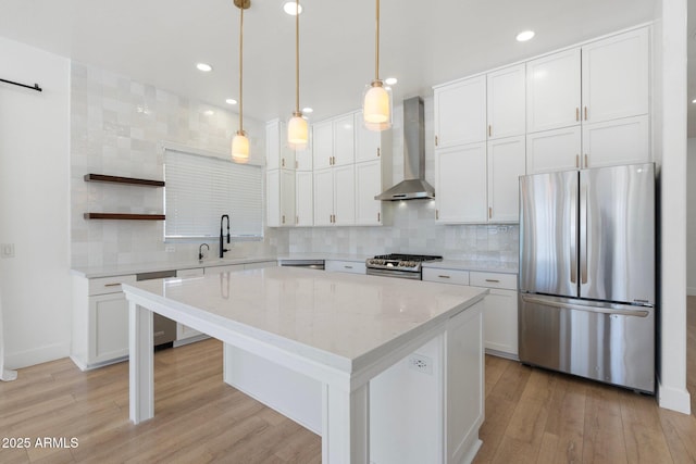 kitchen featuring pendant lighting, wall chimney range hood, stainless steel appliances, white cabinets, and a kitchen island