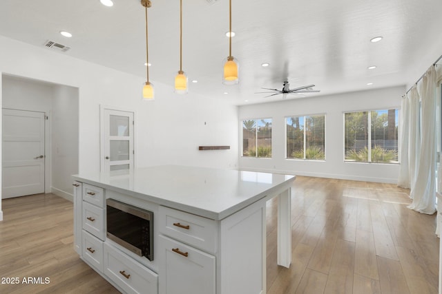 kitchen featuring stainless steel microwave, decorative light fixtures, white cabinets, a center island, and light hardwood / wood-style flooring