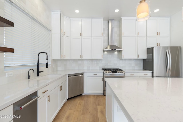 kitchen featuring sink, white cabinetry, hanging light fixtures, stainless steel appliances, and wall chimney exhaust hood