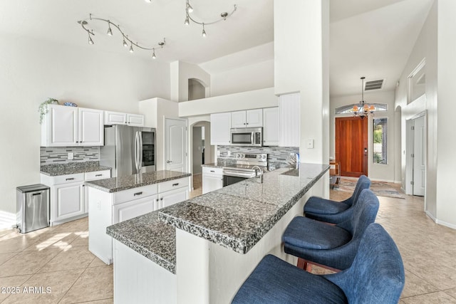 kitchen with appliances with stainless steel finishes, white cabinetry, dark stone counters, decorative backsplash, and kitchen peninsula