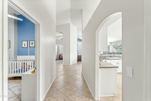 corridor featuring sink, light tile patterned floors, and lofted ceiling