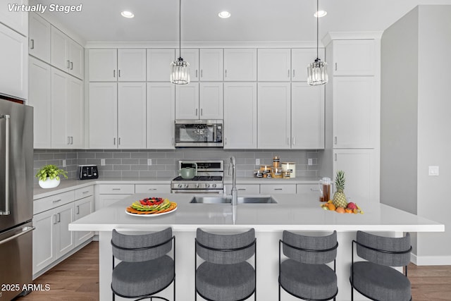 kitchen featuring stainless steel appliances, a kitchen island with sink, a kitchen breakfast bar, and decorative light fixtures