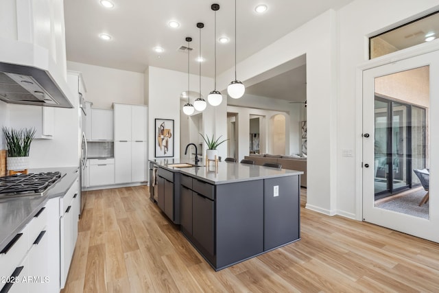 kitchen featuring premium range hood, pendant lighting, white cabinetry, an island with sink, and light hardwood / wood-style flooring