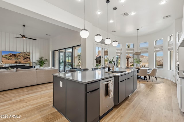 kitchen featuring sink, light hardwood / wood-style flooring, hanging light fixtures, a center island with sink, and stainless steel dishwasher