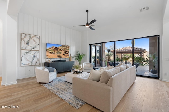 living room with a towering ceiling, light hardwood / wood-style flooring, and ceiling fan