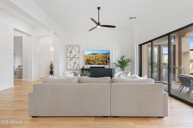 living room with ceiling fan, light hardwood / wood-style flooring, and wood walls