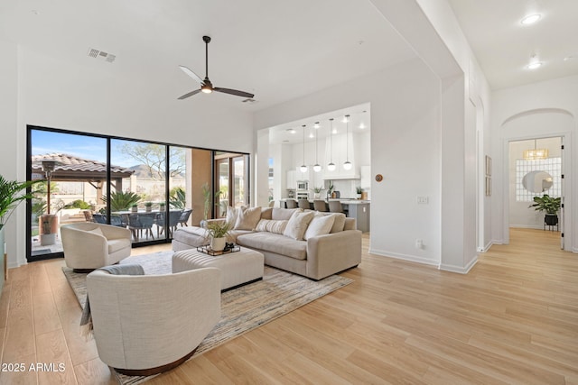 living room featuring a high ceiling, ceiling fan, and light hardwood / wood-style floors