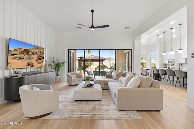 living room with ceiling fan, sink, light hardwood / wood-style floors, and a towering ceiling