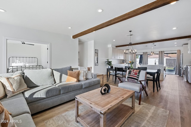 living room with ceiling fan with notable chandelier, beam ceiling, and light wood-type flooring