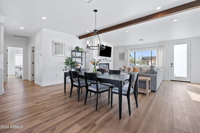 dining area with hardwood / wood-style floors, beamed ceiling, and an inviting chandelier