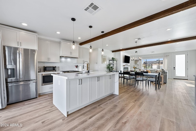 kitchen with beamed ceiling, appliances with stainless steel finishes, hanging light fixtures, and an island with sink