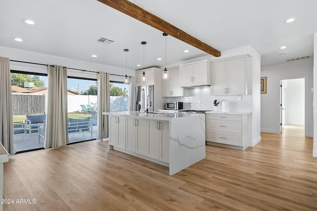 kitchen with a kitchen island with sink, beam ceiling, appliances with stainless steel finishes, light hardwood / wood-style floors, and white cabinetry