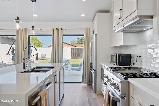 kitchen with light wood-type flooring, stainless steel appliances, sink, white cabinetry, and hanging light fixtures