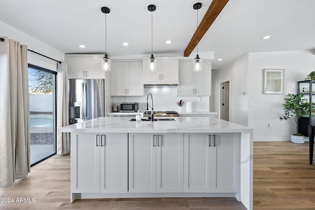 kitchen with white cabinets, a center island with sink, and light stone counters