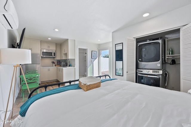 bedroom with a wall mounted AC, hardwood / wood-style flooring, stacked washer / dryer, and sink