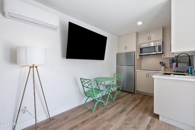 kitchen featuring white cabinetry, sink, stainless steel appliances, a wall mounted air conditioner, and light wood-type flooring