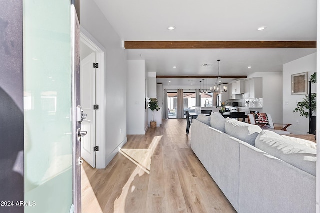 living room with beamed ceiling, light hardwood / wood-style floors, and an inviting chandelier