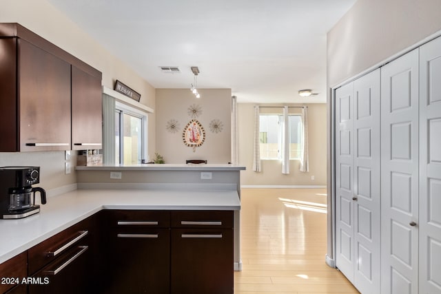 kitchen with pendant lighting, dark brown cabinetry, kitchen peninsula, and light hardwood / wood-style flooring