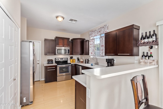 kitchen featuring kitchen peninsula, appliances with stainless steel finishes, light hardwood / wood-style floors, and sink