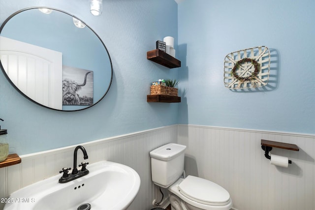 half bath featuring wainscoting, toilet, and a sink