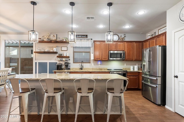 kitchen featuring visible vents, a kitchen island, brown cabinets, wood finished floors, and stainless steel appliances