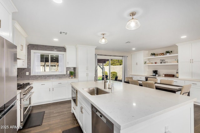 kitchen with sink, appliances with stainless steel finishes, light stone countertops, an island with sink, and white cabinets