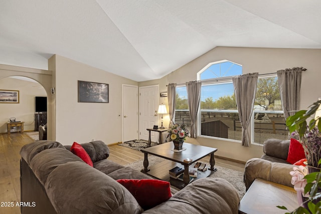 living area with arched walkways, lofted ceiling, a textured ceiling, wood finished floors, and baseboards