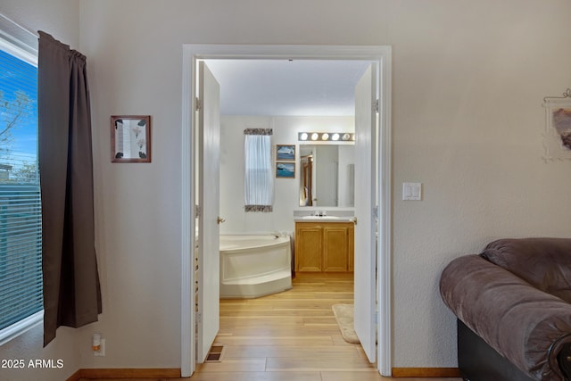 bathroom featuring a garden tub, vanity, baseboards, and wood finished floors