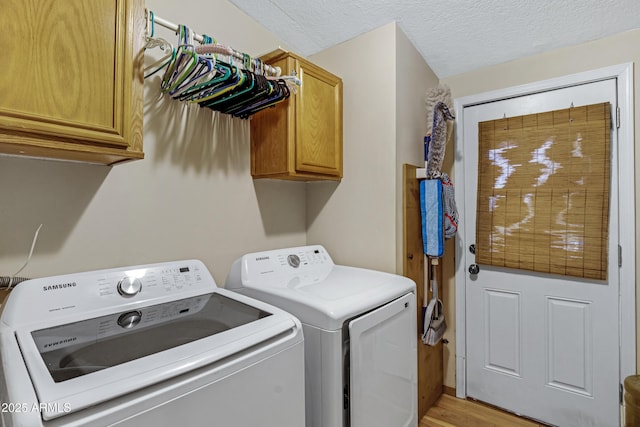 washroom featuring cabinet space, washer and clothes dryer, a textured ceiling, and light wood finished floors