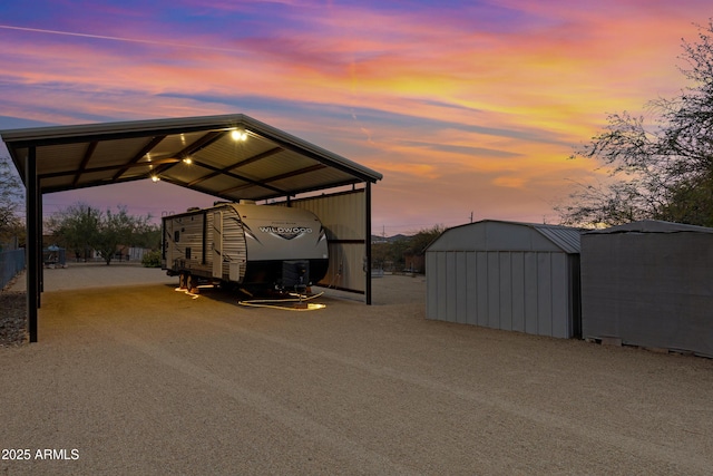 view of parking featuring a carport, a storage unit, and gravel driveway