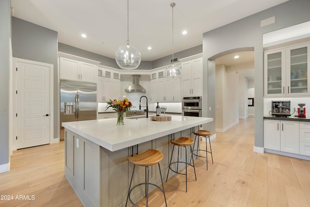 kitchen featuring white cabinetry, appliances with stainless steel finishes, wall chimney exhaust hood, decorative light fixtures, and light wood-type flooring