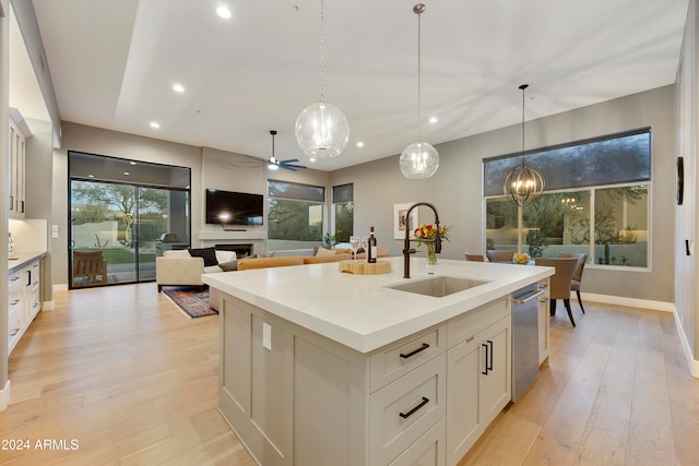 kitchen featuring light hardwood / wood-style floors, sink, an island with sink, hanging light fixtures, and dishwasher