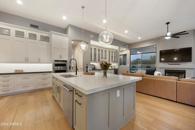 kitchen with stainless steel appliances, light hardwood / wood-style floors, an island with sink, hanging light fixtures, and white cabinets