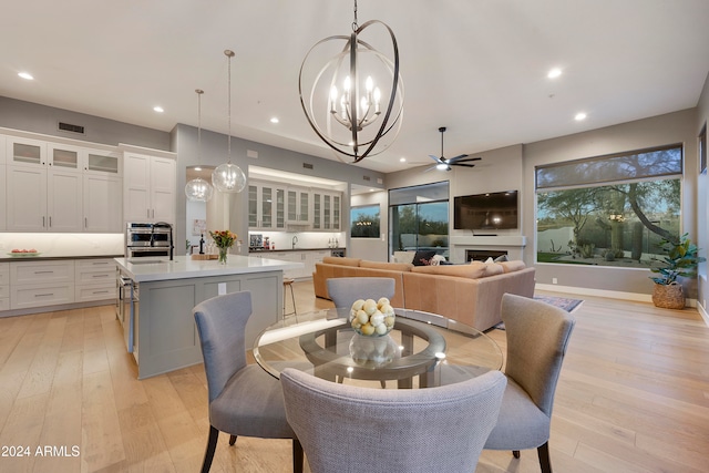 dining space with light wood-type flooring, sink, and ceiling fan with notable chandelier