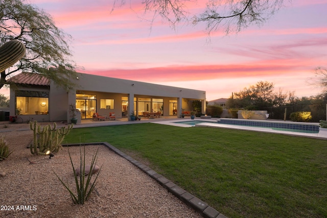 back house at dusk with a yard and a patio