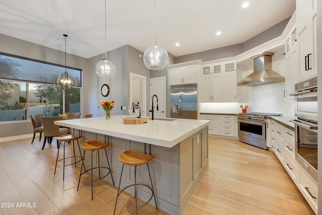 kitchen with sink, a large island with sink, wall chimney exhaust hood, high end appliances, and light hardwood / wood-style flooring