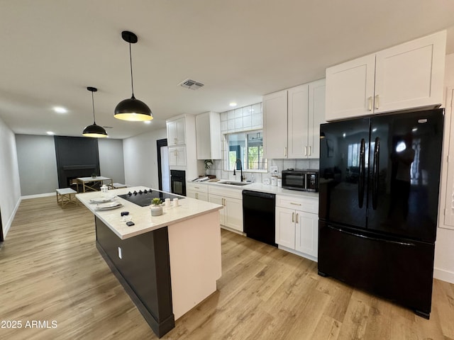 kitchen featuring black appliances, a sink, white cabinets, light wood finished floors, and a kitchen island