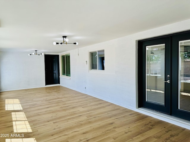 unfurnished room featuring a chandelier, light wood-style flooring, brick wall, and french doors
