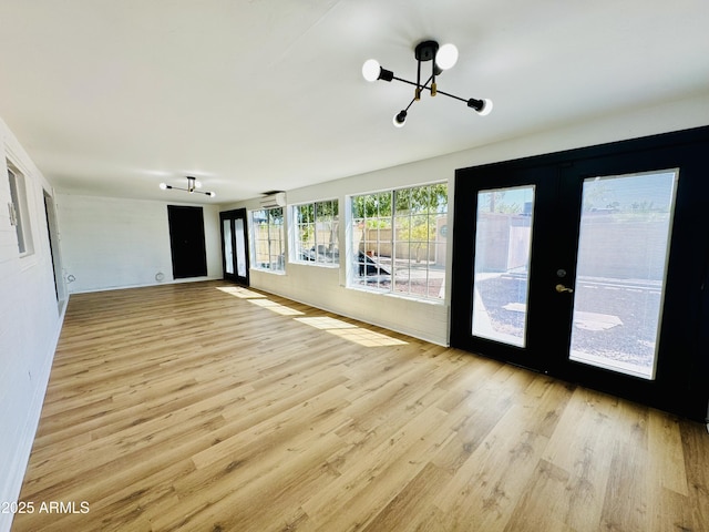 unfurnished living room with a chandelier, french doors, and light wood finished floors