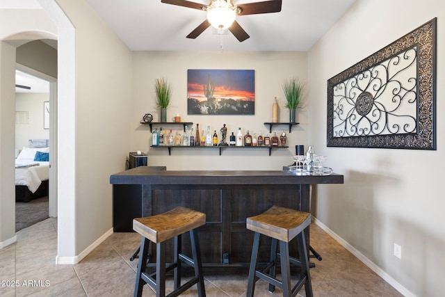 bar with arched walkways, ceiling fan, a bar, and tile patterned flooring