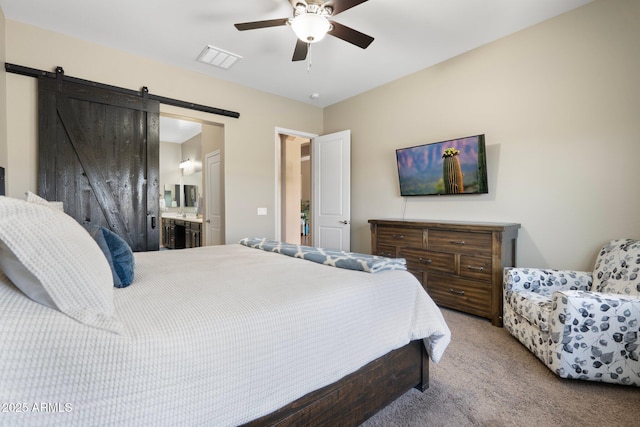 carpeted bedroom with ensuite bathroom, a barn door, a ceiling fan, and visible vents