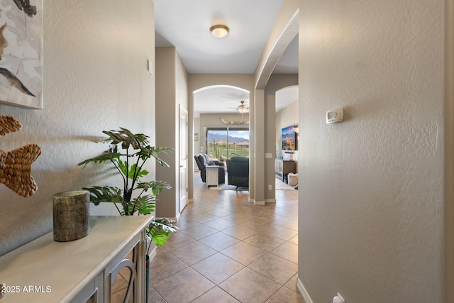 hall featuring arched walkways, baseboards, a textured wall, and light tile patterned floors