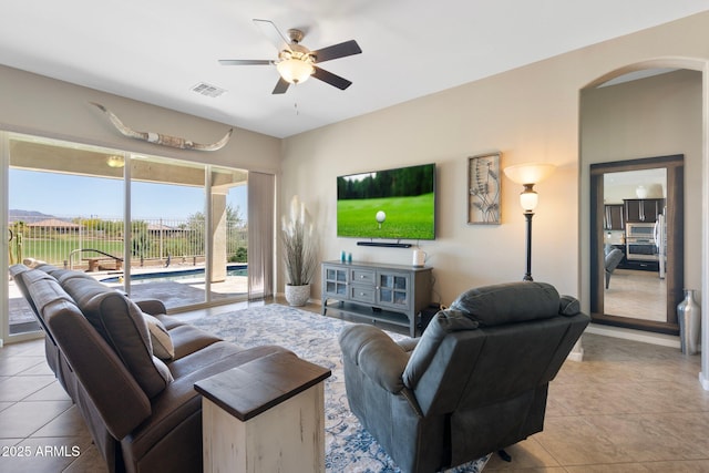 tiled living room featuring arched walkways, ceiling fan, and visible vents