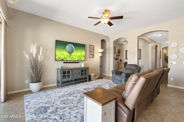 living area with baseboards, arched walkways, ceiling fan, and light tile patterned flooring
