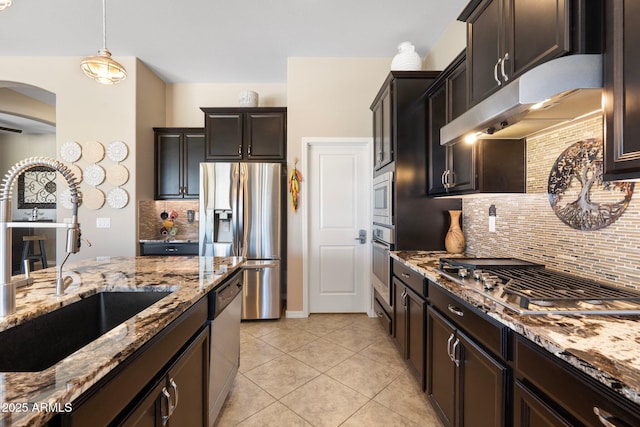 kitchen with arched walkways, light stone countertops, a sink, under cabinet range hood, and stainless steel appliances