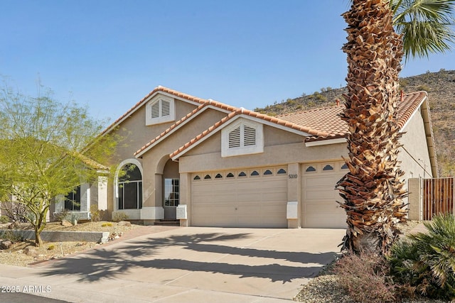 mediterranean / spanish home featuring concrete driveway, an attached garage, a tiled roof, and stucco siding